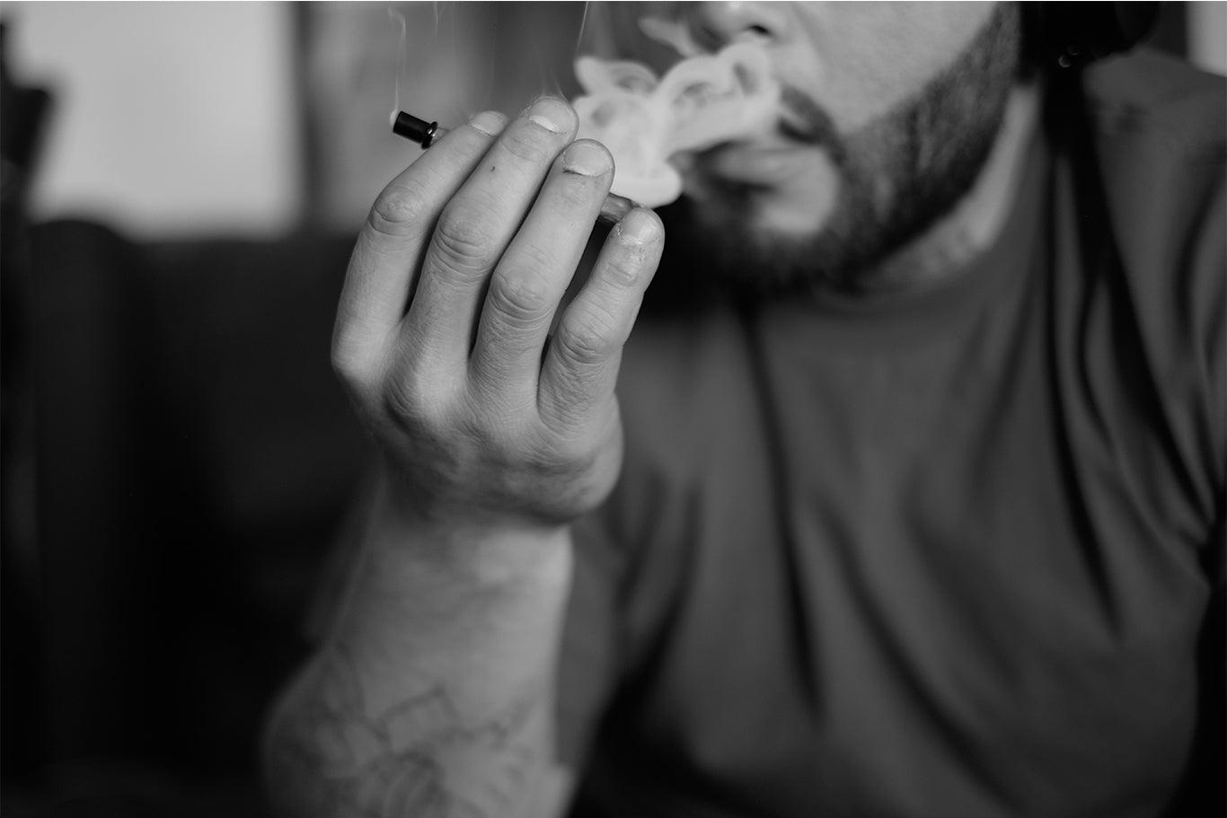 Una persona con la barba porta alla bocca un blunt